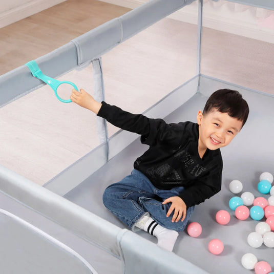 Corral de juego color gris con tapete didáctico de dobleces, hecho en material resistente, con laterales en malla, puerta con cierre para facilitar el ingreso, incluye pelotitas y dos agarraderas